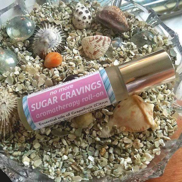 No More Sugar Cravings essential oil roll-on bottle on a bed of natural stones and seashells, promoting energy and metabolism.
