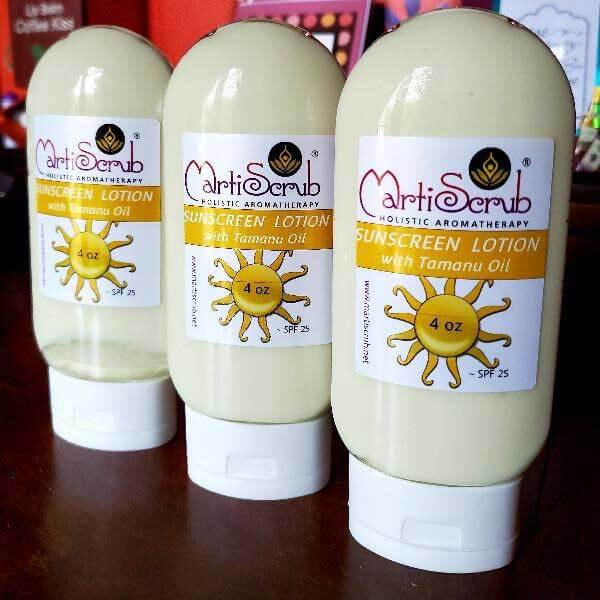Three 4 oz bottles of MartiScrub Sunscreen Lotion with Tamanu Oil, SPF 25, on a wooden surface.