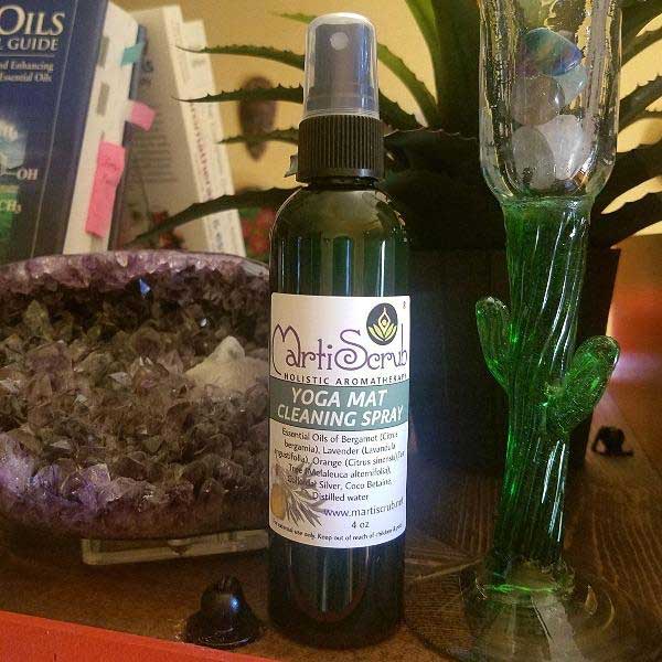 Yoga mat cleaning spray bottle with essential oils on a table surrounded by plants and crystals.