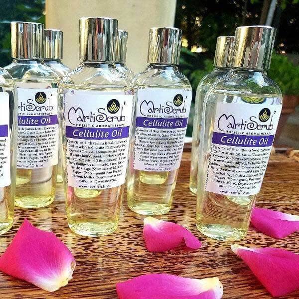 Bottles of MartiScrub Cellulite Oil on a wooden surface with rose petals, featuring essential oil blend for reducing cellulite.